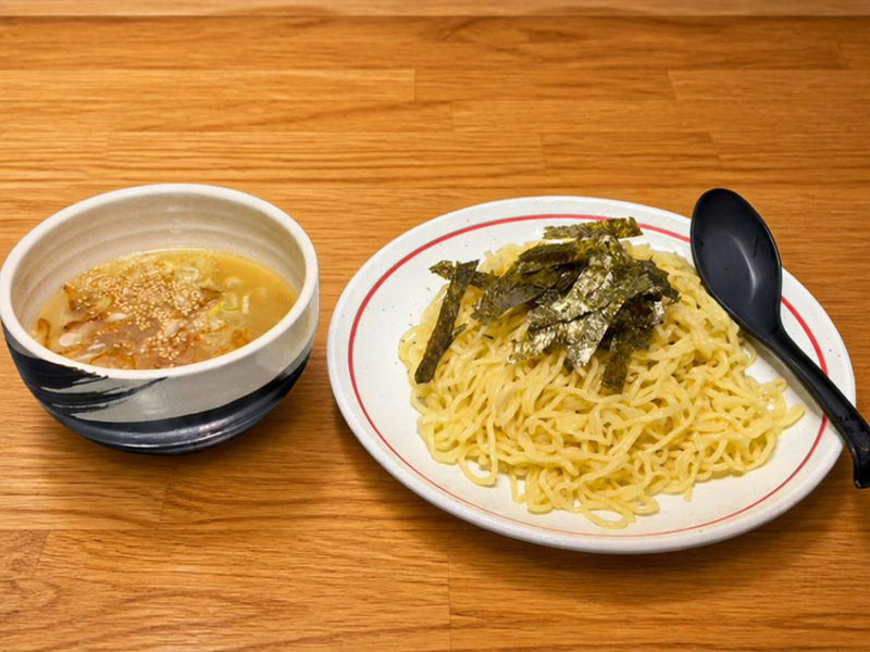 富士市でつけ麺・ラーメンを提供する「つけ麺処Sin 富士本店」の看板メニュー、鶏塩つけ麺。木目のテーブルに置かれた、ネギが浮かぶ透明感のある鶏塩スープと、海苔が添えられた艶やかな麺。