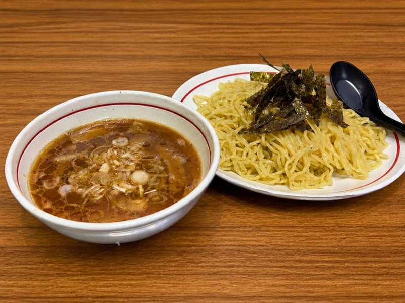 富士市でつけ麺・ラーメンを提供する「つけ麺処Sin 富士本店」の定番メニュー、鶏醤油つけ麺。木目のテーブルに置かれた、ネギが浮かぶ風味豊かな鶏醤油スープと、海苔が添えられた艶やかな麺。