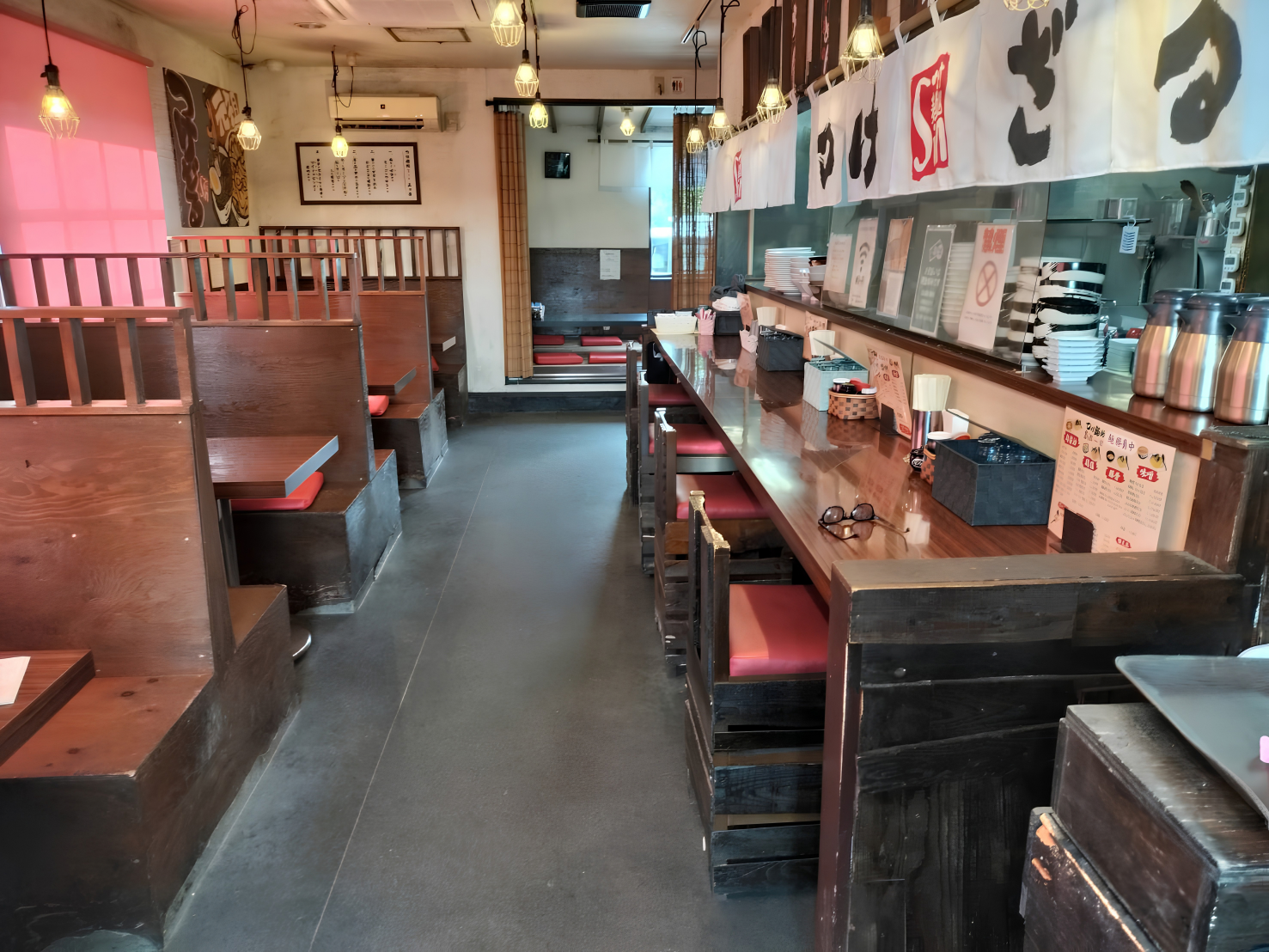 富士市のつけ麺店「つけ麺処Sin 富士本店」の店内風景。木目を基調とした温かみのある空間に、のれんが掛かったカウンター席と、赤い座布団のボックス席が並んでいます。